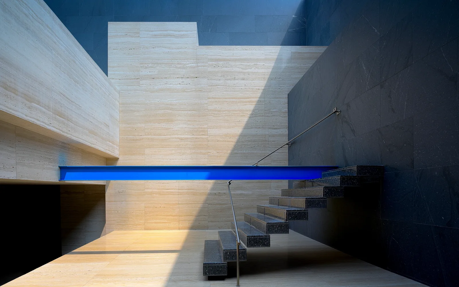 Minimalist Milanese architectural stone staircase intersected by an ultramarine structural beam.