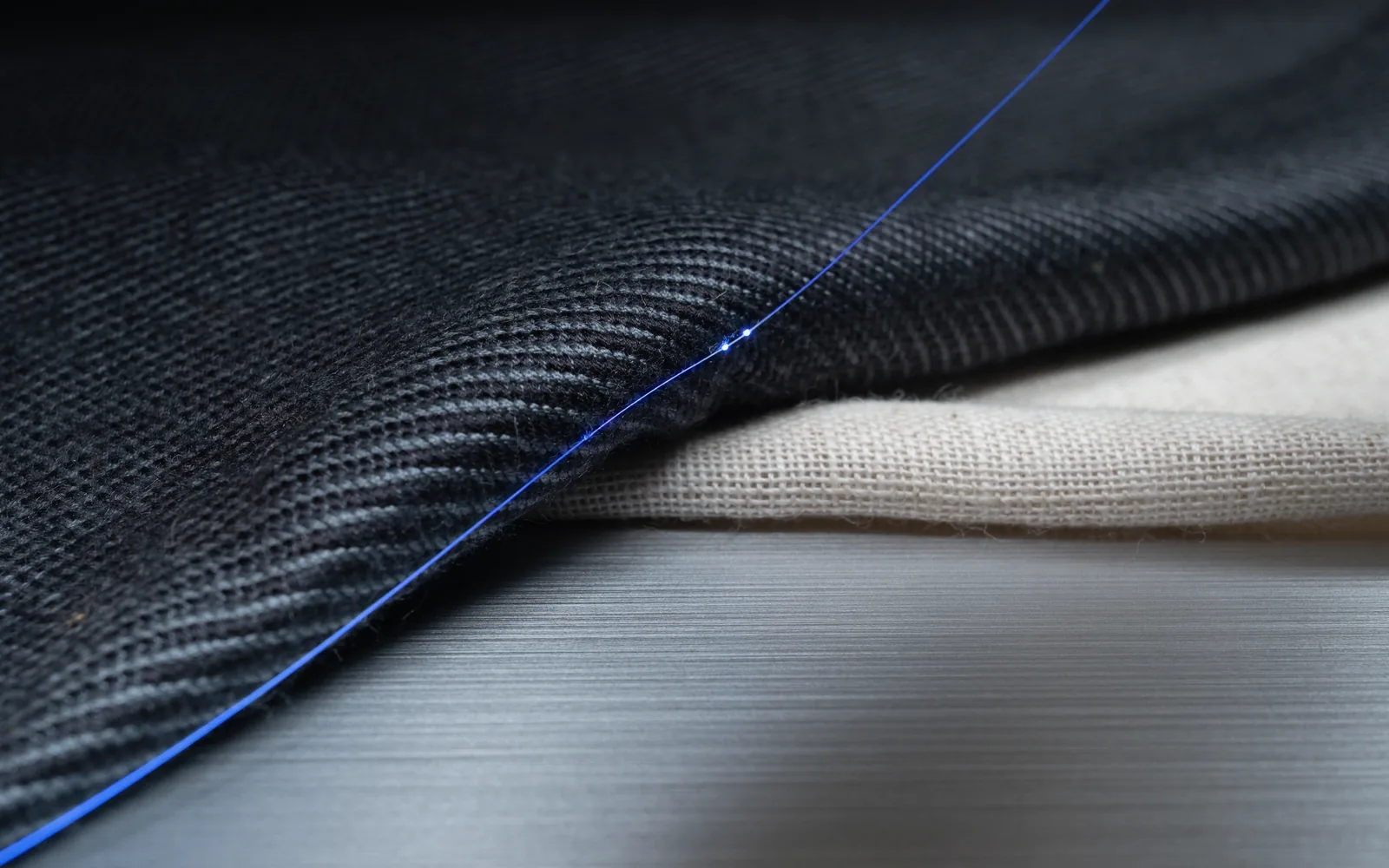 Architectural dark wool-silk weave intersected by a luminous ultramarine optical fiber thread.