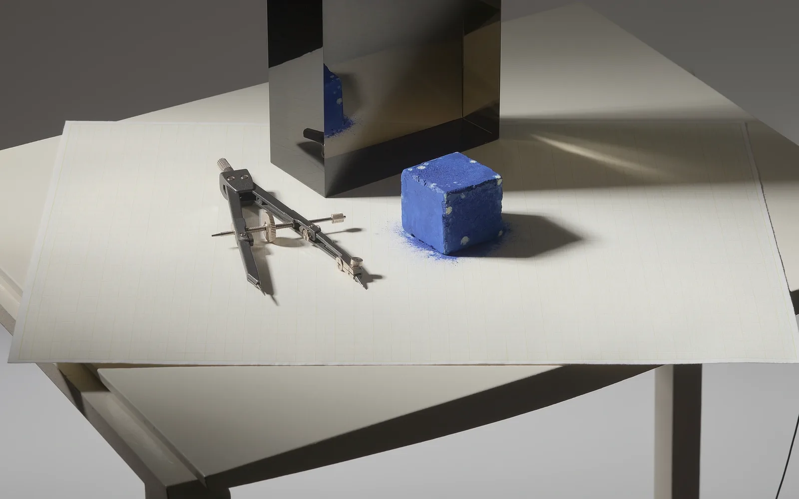 Overhead composition of architectural grid paper, drafting instruments and raw ultramarine pigment.